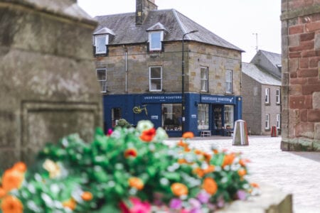 Blue-fronted Ynortheous Roasters shopfront on a stone corner building beyond flowers