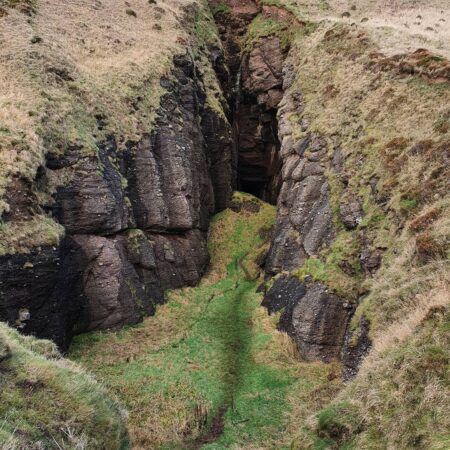 Narrow rocky gorge with moss-covered floor cutting through grassy hillside