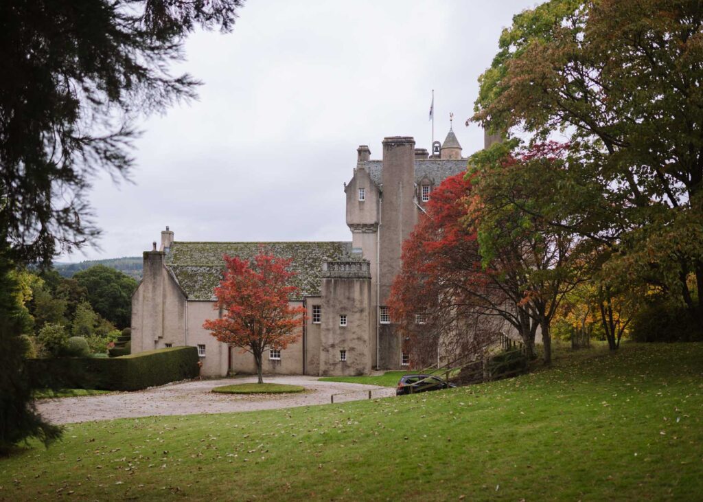 Turreted stone castle with flag pole, surrounded by autumn trees and lawns