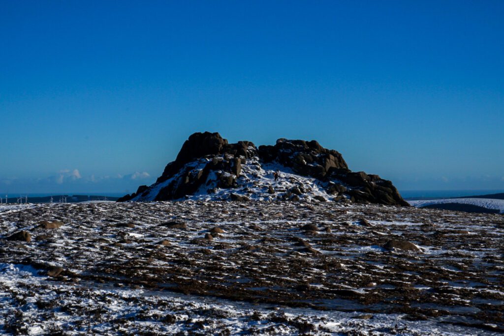 The granite tor on the top of Clachnaben in snow, under a deep blue sky.