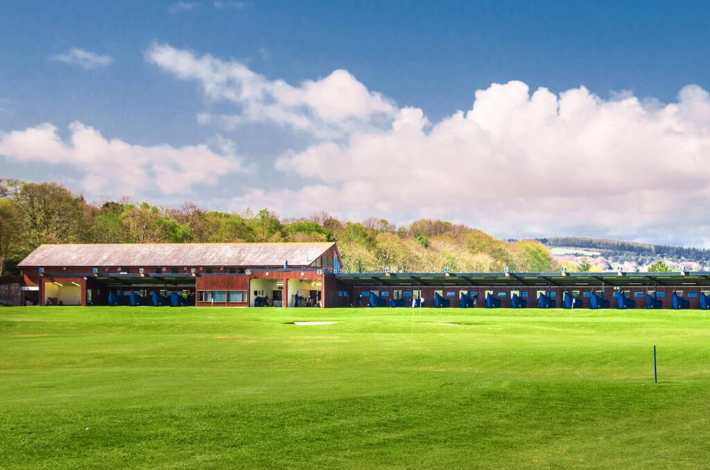 Golf driving range with covered bays overlooking a putting green and trees