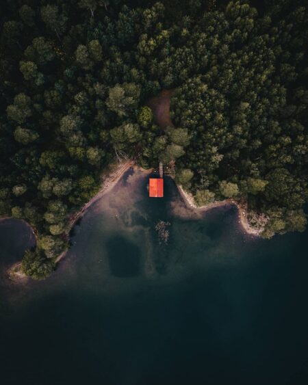 Aerial view of a red-roofed cabin on a forested loch shore