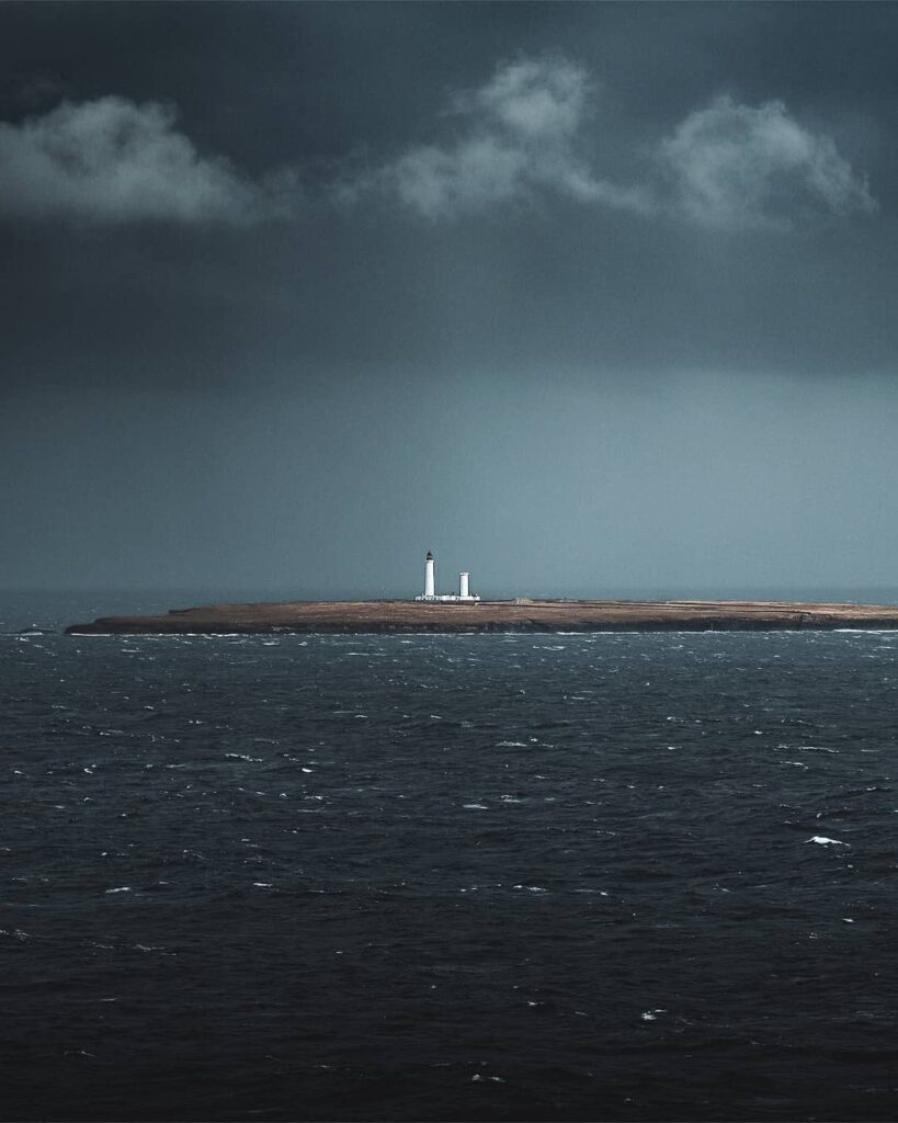 White lighthouses on a low island under dark, storm-laden clouds