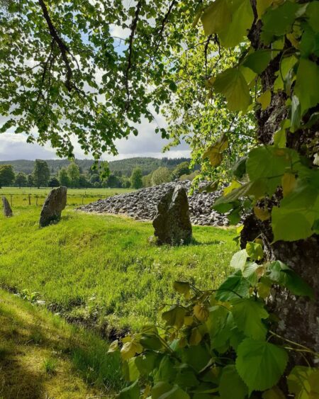Standing stones and cairn at Balnuaran of Clava, framed by tree leaves