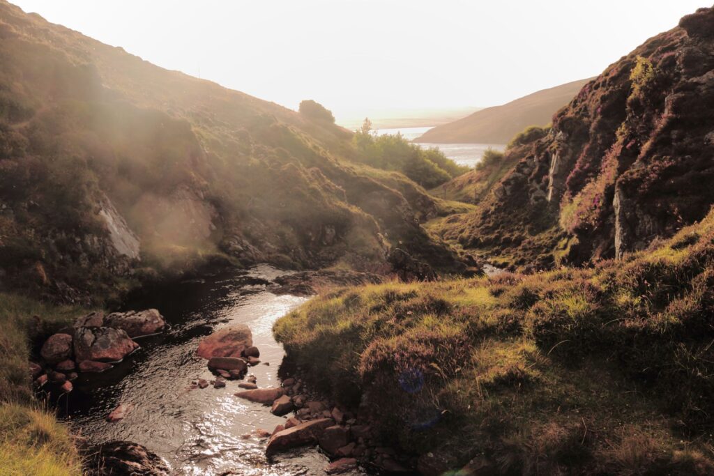Low sun through the Valayre ravine, the burn shining over red stones.