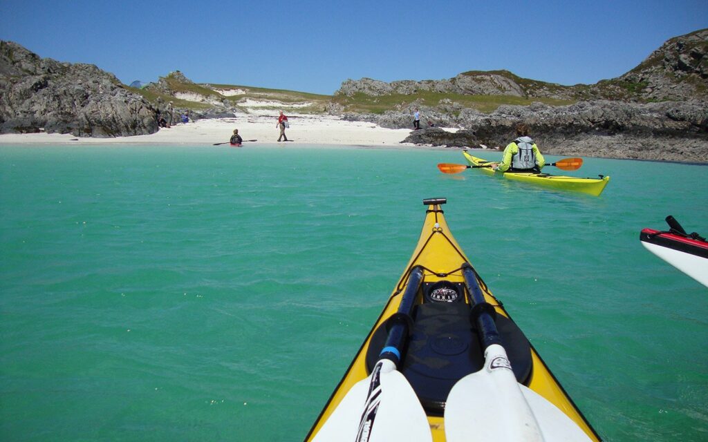 Kayaks crossing turquoise water towards a white sandy beach between rocky headlands