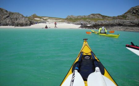 Kayaks crossing turquoise water towards a white sandy beach between rocky headlands