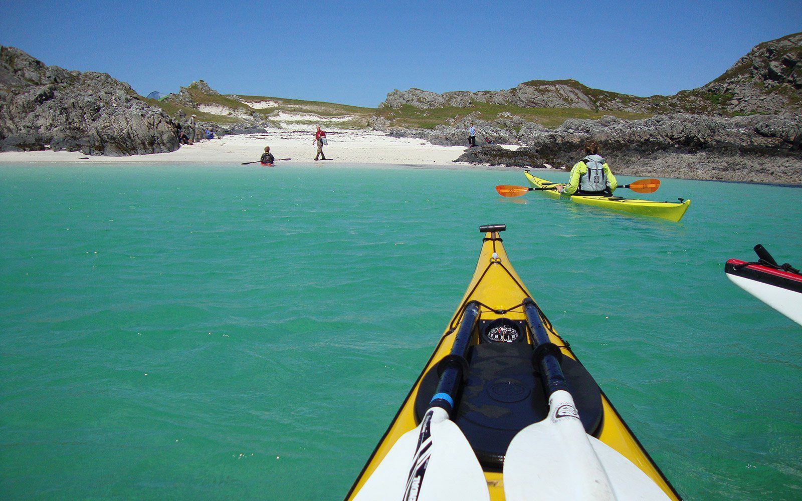 Kayaks crossing turquoise water towards a white sandy beach between rocky headlands