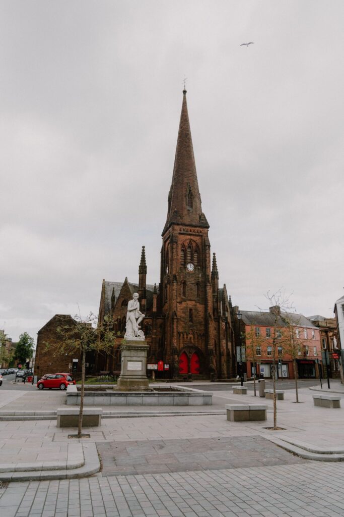 Sandstone church spire with clock tower overlooks a statue in Dumfries town square