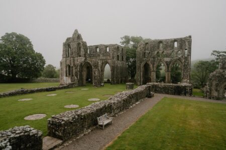 Ruined stone abbey arches rise above misty grounds with a stone bench