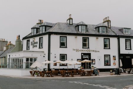 The Harbour House Hotel with white walls, dormer windows and outdoor tables shaded by parasols