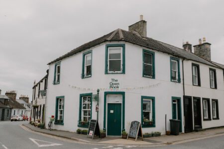 White corner building with green trim on a street corner, signed The Open Book