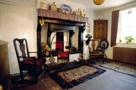 Cottage room with black cast-iron range, tartan mantel and spinning wheel beside the window