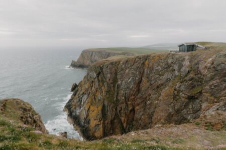 Small wooden hut atop layered coastal cliffs above the sea