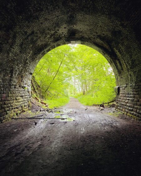 Brick archway of a disused railway tunnel framing a wooded path beyond