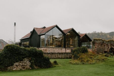 Glass-fronted distillery buildings beside a ruined stone wall and chimney