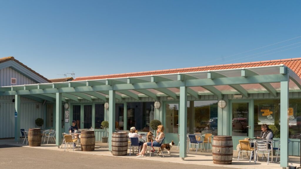 Diners sit under a covered pergola beside barrel tables outside a café