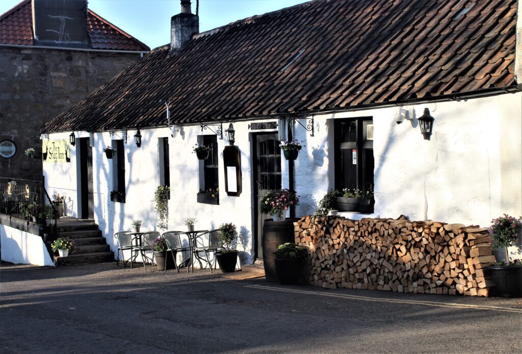 Whitewashed cottage pub with pantiled roof, hanging lanterns and a stacked woodpile outside