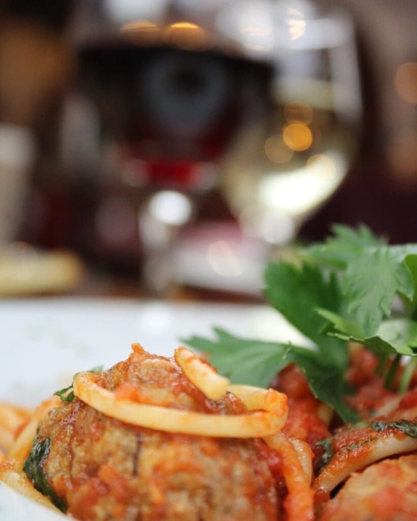 A pasta dish with herbs beside glasses of wine.