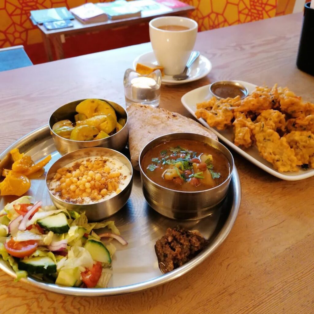 A thali of curries, rice, salad and pakoras on a table.
