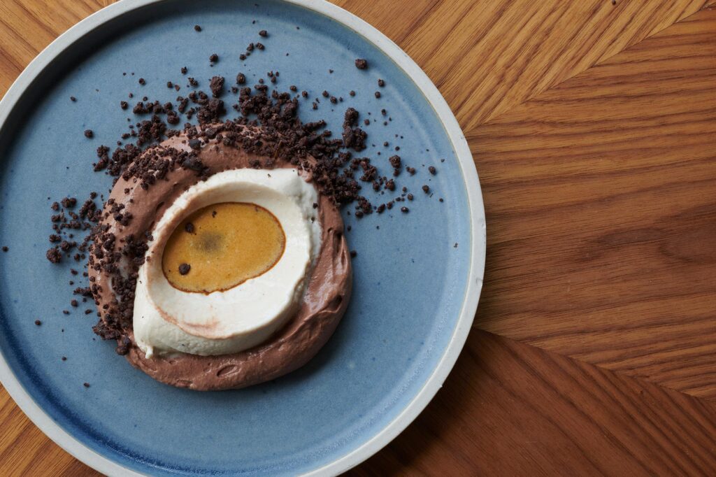 A chocolate dessert with a coffee cream centre and cocoa crumb on a blue plate.