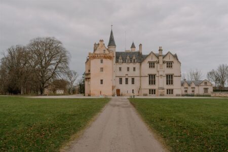 Gravel path leads to a turreted Scottish castle under grey skies