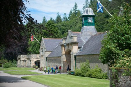 Visitors walk past a stable block with clock tower and Saltire flag