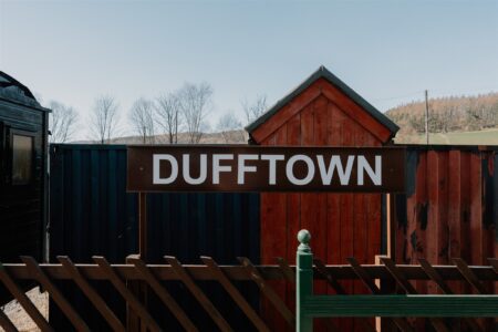 Dufftown station sign mounted on a wooden shed with railway carriage alongside