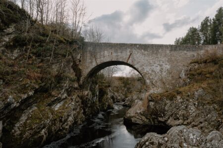 Stone arched bridge spanning a rocky gorge with a narrow river below