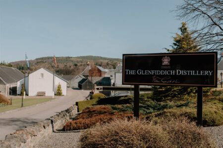 The Glenfiddich Distillery sign beside whitewashed buildings and a stone wall