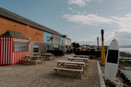 Picnic tables and a striped kiosk beside a paddleboard on the shore