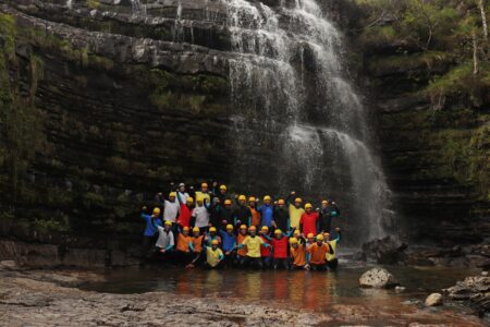 Group in yellow helmets and coloured jackets posing beneath a cascading waterfall
