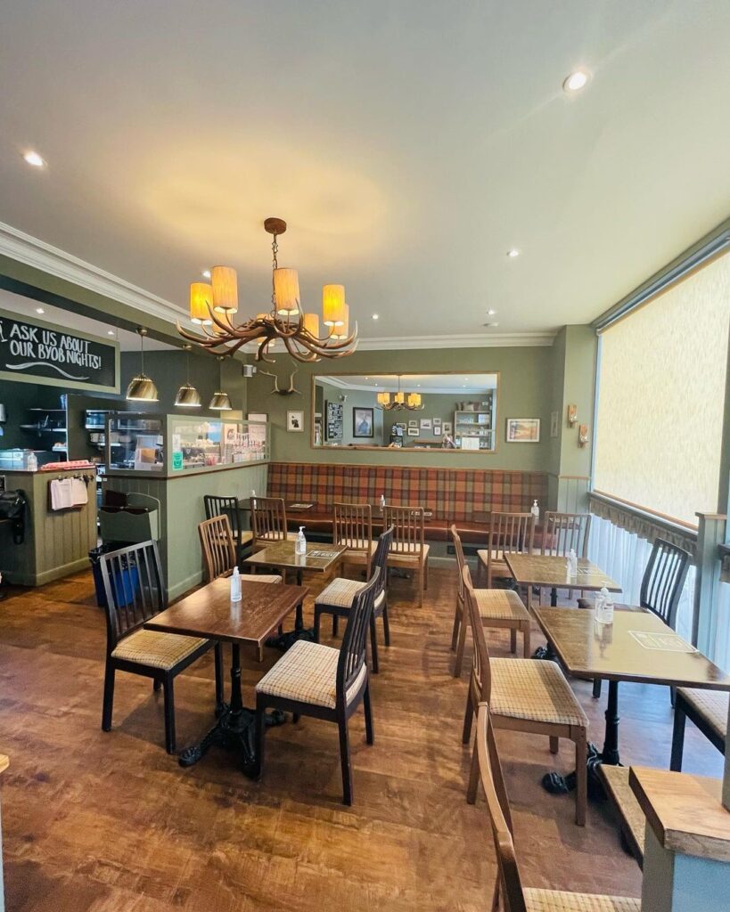 Tartan booth seating and wooden tables beneath an antler chandelier in a café