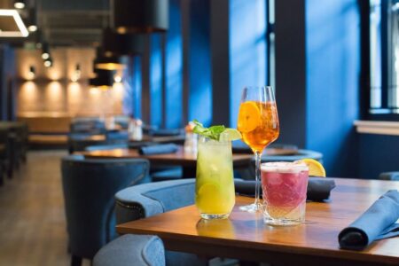 Three cocktails on a wooden table in a dimly lit restaurant