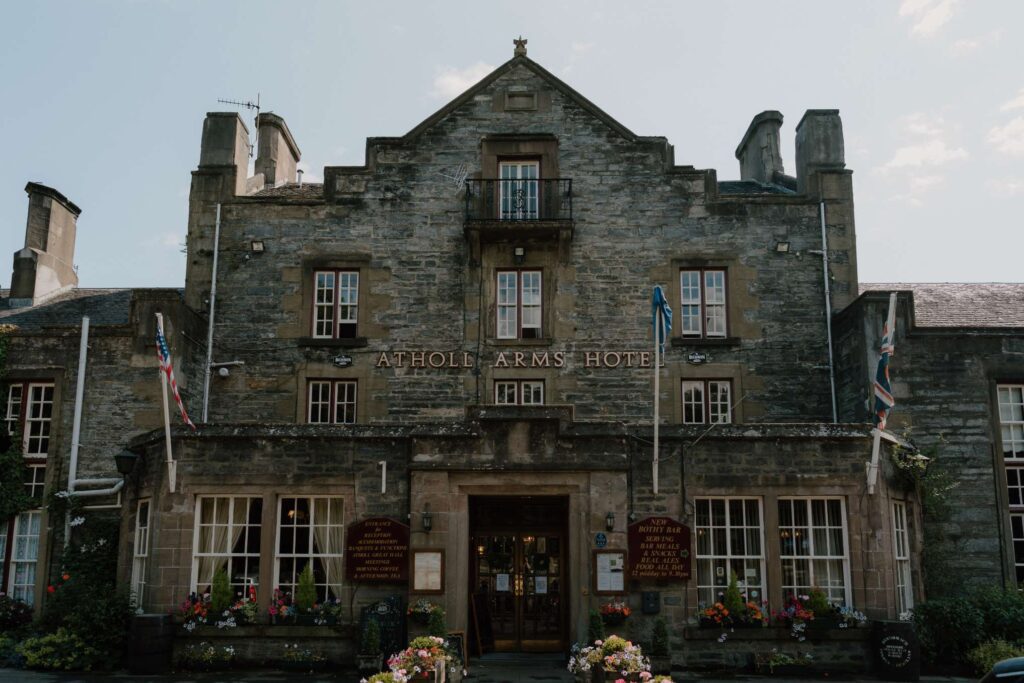 Stone facade of the Atholl Arms Hotel with flags and flower baskets