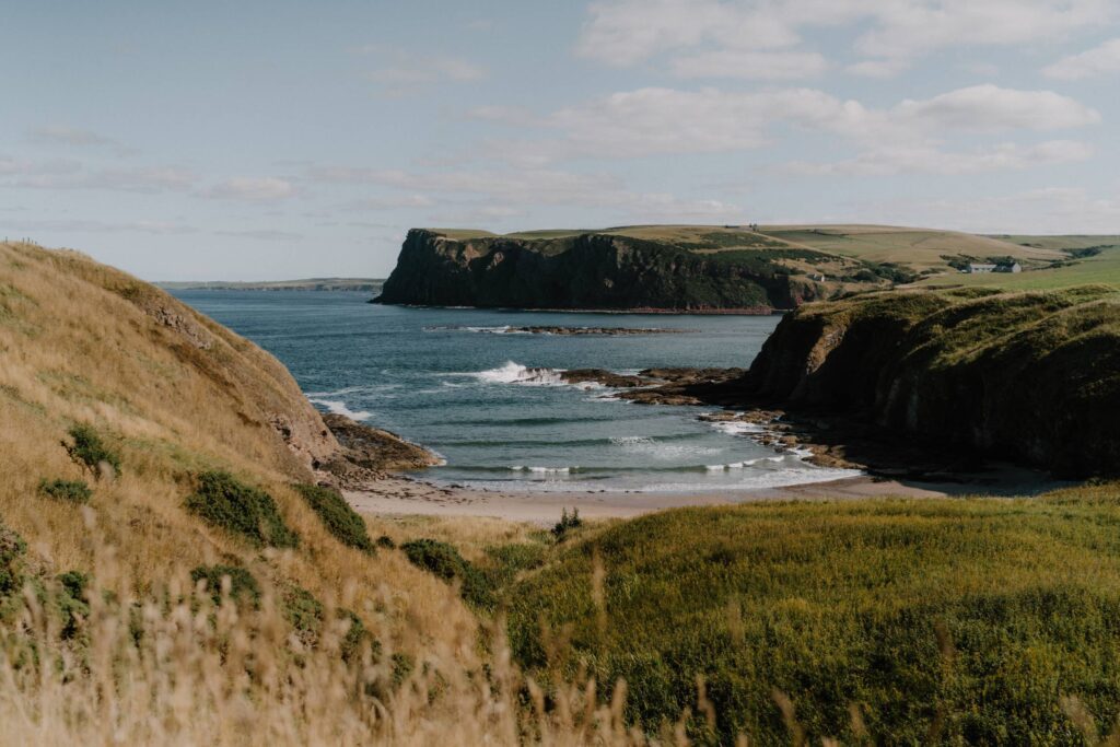 Grassy headlands enclose a small sandy beach with gentle waves