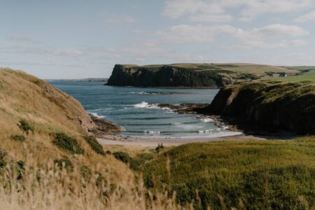 Grassy headlands enclose a small sandy beach with gentle waves