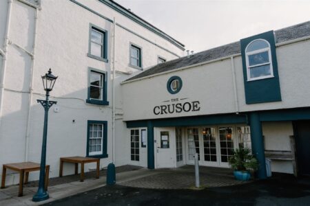 White building entrance with dark green trim reading "The Crusoe" above glass doors