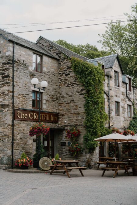 The Old Mill Inn's stone façade covered in ivy, with picnic tables outside