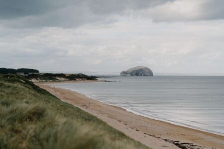 Grassy dunes overlook a curving sandy beach with Bass Rock offshore