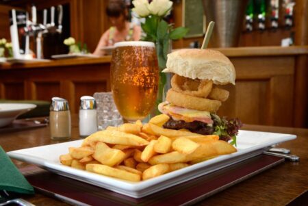Burger stacked with onion rings, chips and a pint of beer at the bar