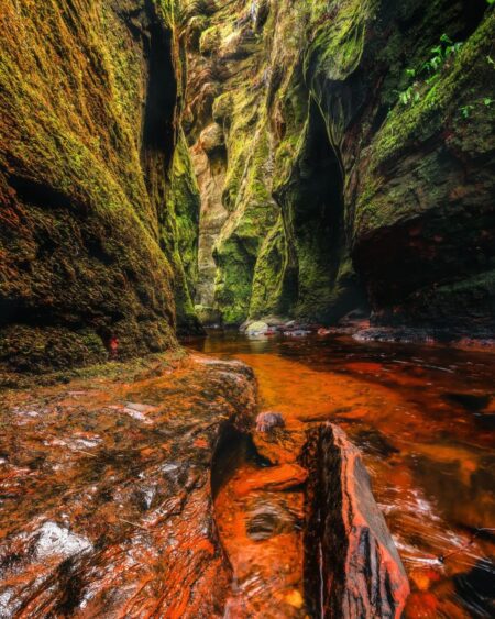 Rust-coloured water flows through the narrow, moss-covered walls of Finnich Glen