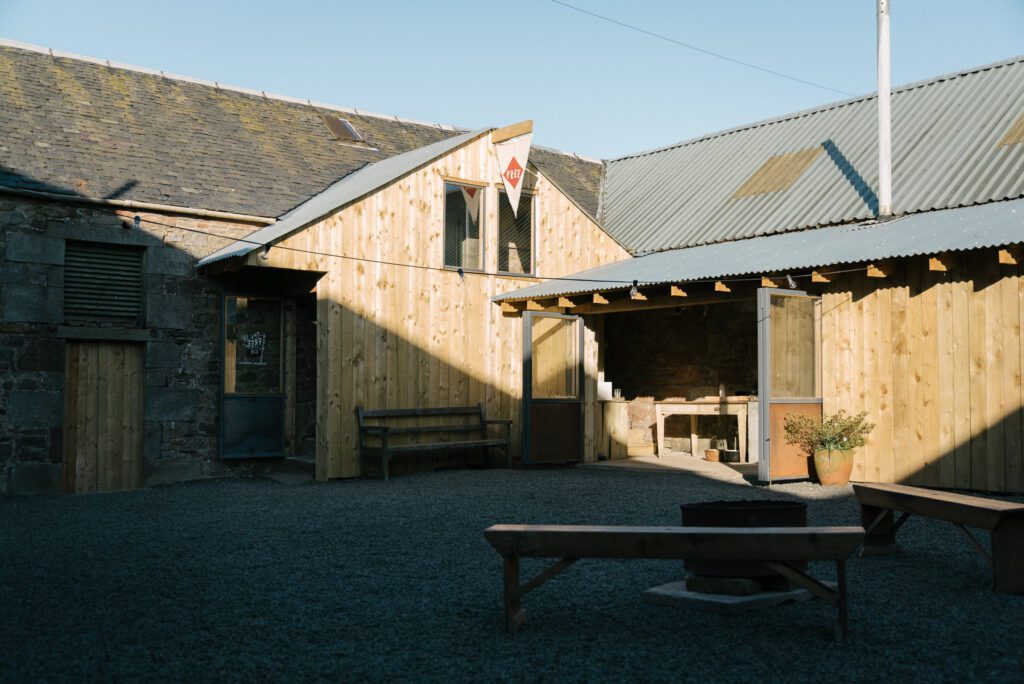 Timber-clad courtyard buildings with corrugated roofs and a gravelled seating area