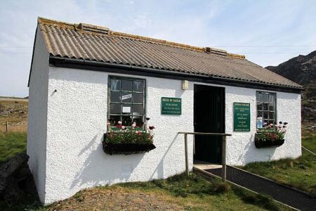 The white Colonsay Bookshop at Scalasaig, window boxes of flowers under its windows.