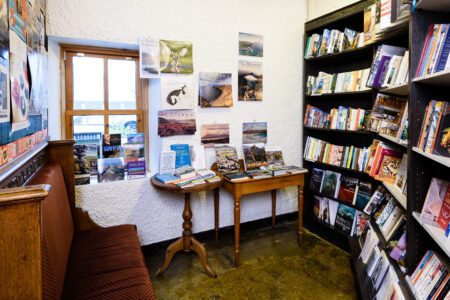 Bookshop corner with postcards pinned above tables and crowded shelves