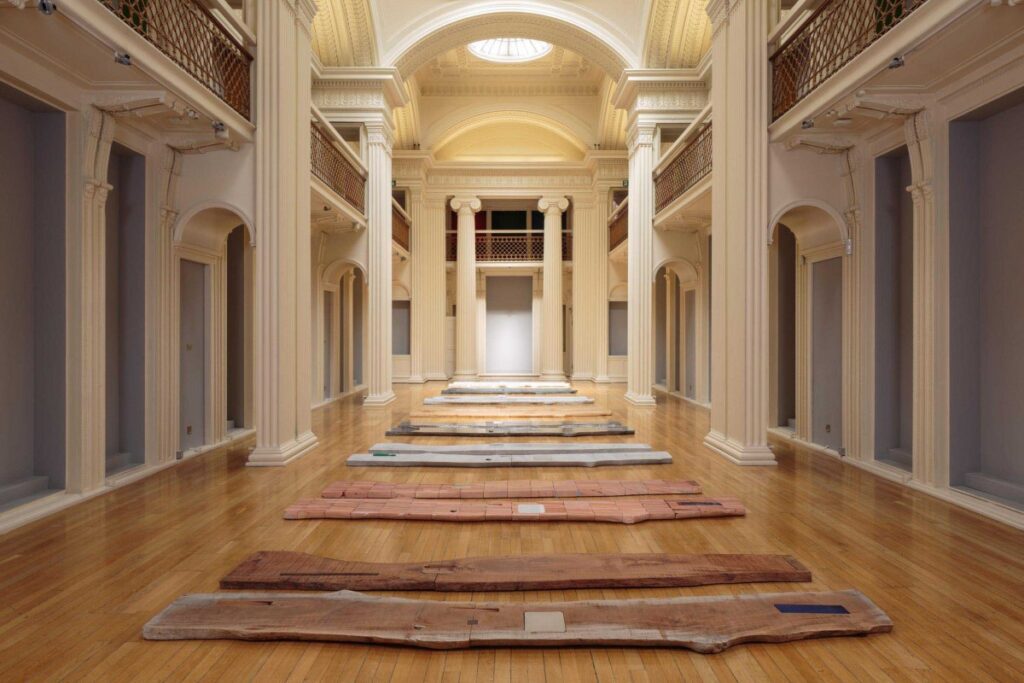 Timber slabs laid along the wooden floor of a grand columned gallery