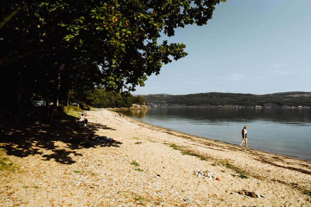 A walker on Ardentinny Beach under the trees.