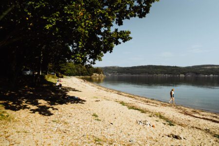 A walker on Ardentinny Beach under the trees.