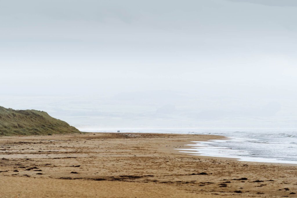 The long curve of Westport Beach running south into haze, the surf breaking.
