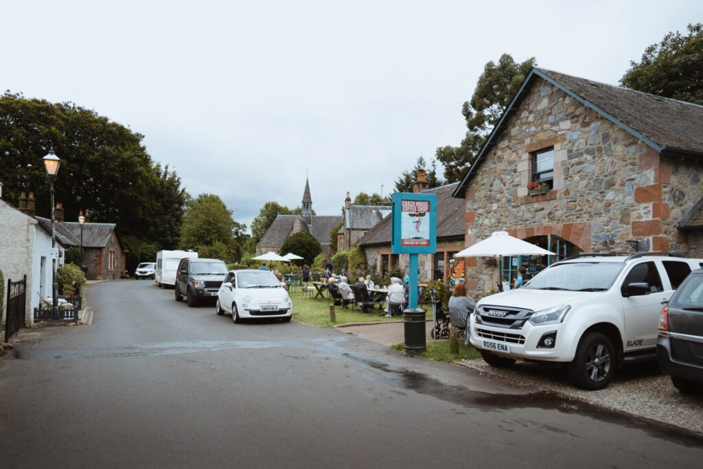 Church Road in Luss, the café's sign by the street and the church spire beyond.